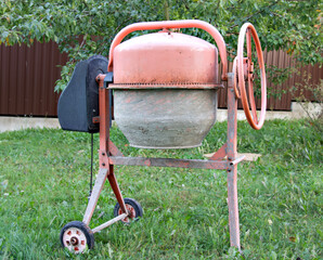A concrete mixer stands against a background of green grass. Close-up