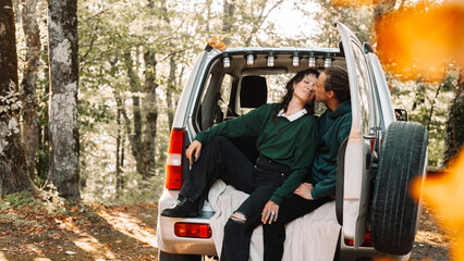 A man and a woman are sitting in the trunk of a car and kissing in the autumn forest.