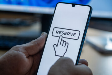 “Reserved” message on close-up smartphone screen. Online reservation. Office background. Hotel, vacation or event booking message. 