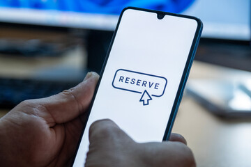 “Reserved” message on close-up smartphone screen. Online reservation. Office background. Hotel, vacation or event booking message. 