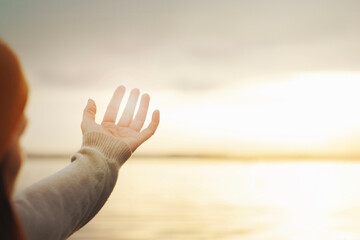 person filters with his hand the warm light of the sun at sunset on the sea, concept of energy and freedom