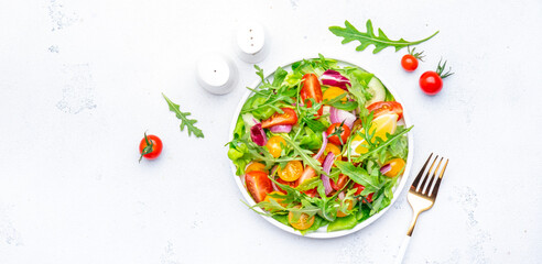 Vegan vegetable salad with red and yellow tomatoes, cucumber, red onion, green lettuce and arugula. White background, top view