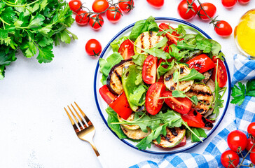 Vegan grilled salad with zucchini, eggplant, paprika, fresh tomatoes and arugula with olive oil. White background, top view