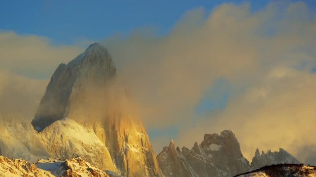 Clouds over Mount Fitz Roy at sunrise with beautiful golden light iluminating the vertical granite walls, El Chalten, Argentina.