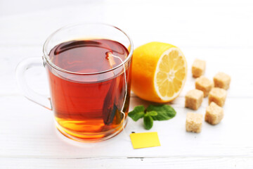 Cup of tea with sugar cubes, lemon and mint leafs on white wooden table
