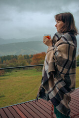 Girl with hot tea in checkered plaid on foggy mountains landscape. Traveler resting in autumn...