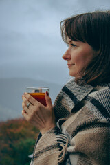 Girl with hot tea in checkered plaid on foggy mountains landscape. Traveler resting in autumn...