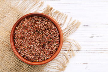 Flax seeds in brown bowl on white wooden background