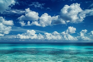 Obraz premium A serene scene of the clear blue sky and turquoise ocean, with fluffy white clouds in the background. The water is crystal clear, reflecting the vibrant colors of the sky above it. 