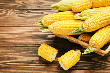 Ripe corn in basket on brown wooden table