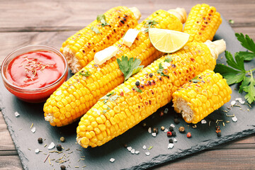 Tasty grilled corn with lime, spices and red sauce on wooden table