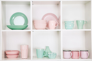 Cupboard shelves in wooden rack with pink and green kitchen dishes close up