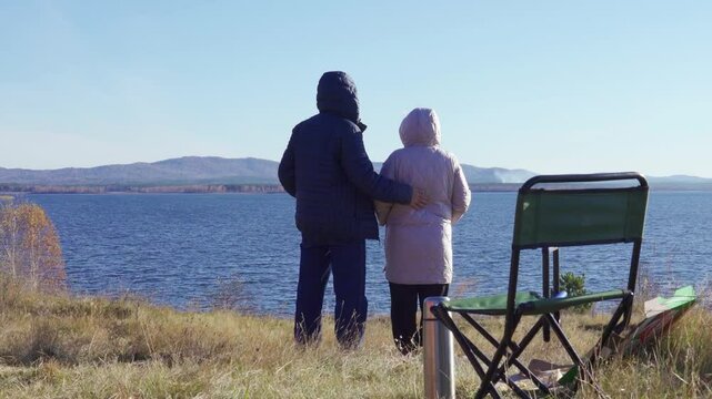 An elderly couple, standing on the shore of a forest lake, admires the wild landscape