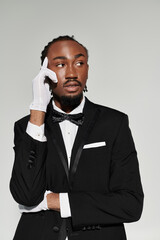 A young African American man in a refined suit and gloves confidently poses against a muted grey background.