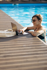 Woman in pool working on laptop standing on the deck