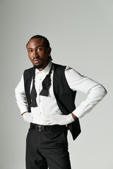 A young African American man dressed in a stylish suit and vest strikes a confident pose with a grey background.