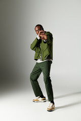 A young African American man strikes a confident pose in fashionable green attire, showcasing his style.