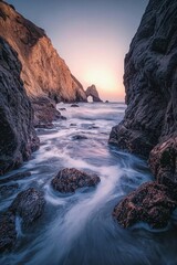 Obraz premium Long-exposure shot of water flowing down the rocks at golden hour, showcasing dramatic shapes and colors at a beach.