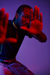 A young man shows his fashion flair with neon lighting while striking a confident pose in the studio.