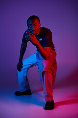 A young man showcases his fashion sense in a studio, illuminated by striking neon lights.