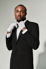 A young man in a sharp suit adjusts his attire, exuding confidence against a smooth grey backdrop.