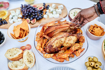 Close up of unrecognizable African American man putting delicious roasted chicken dish with golden potatoes on dining table set for party copy space