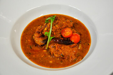 Red Spicy Indian hot chicken curry garnished with vibrant cherry tomatoes, fresh herbs, and dried chili.