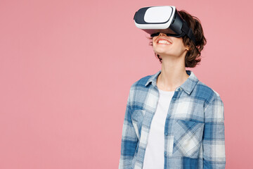 Young smiling woman she wear blue shirt white t-shirt casual clothes watching in vr headset pc gadget look overhead isolated on plain pastel light pink background studio portrait. Lifestyle concept.