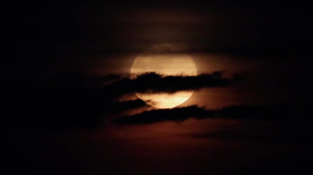 Full moon in the night sky hidden behind dark clouds. Gloomy night landscape on Halloween evening