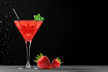 Strawberry summer cocktail drink in a glass with ice and orange on a gray bar counter with black background