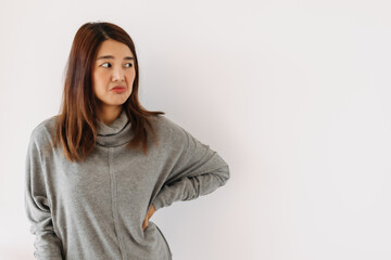 Bored face of asian Thai woman wear grey sweater, pursing mouth and thumbs down, giving bad negative, boring, dislike isolated over white wall.