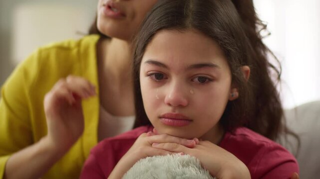 Close up Caucasian crying sad anxious depressed little girl child kid daughter cry upset by school problems abuse bullying while caring loving mother sister woman female comforting stroke hair indoors