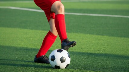 Fototapeta premium Player in red about to kick a soccer ball on a green field.