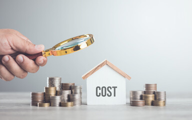 Stack of coins, a house model, and a hand holding a magnifying glass. The concept of evaluating...