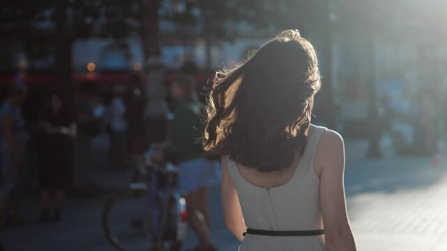 Beautiful woman walking on the street of Paris, in a white summer dress, towards the sun, angle from behind