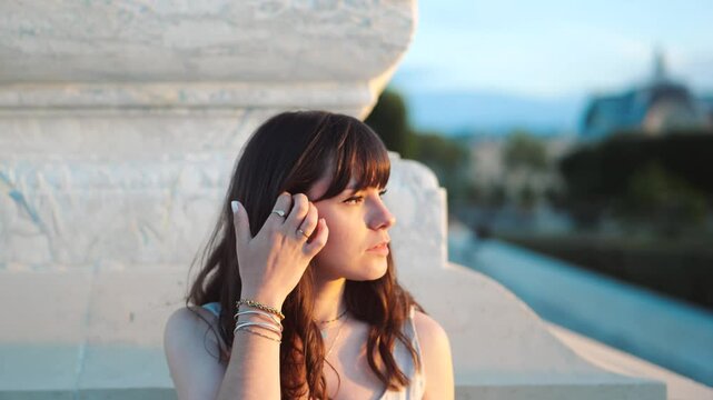 Close up of a beautiful french woman in a park, looking at the sunset while touching her hair, in Paris