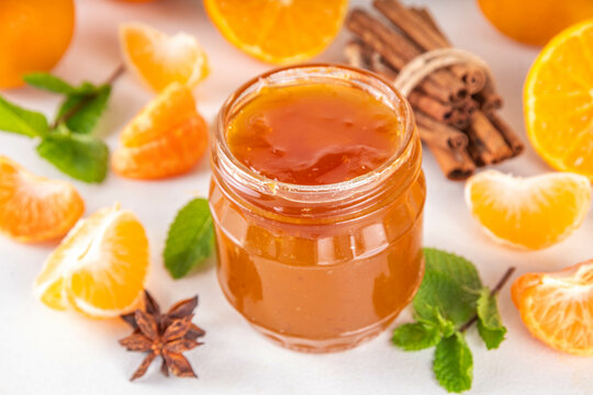 Golden sweet homemade tangerine jam, with spices and mint.  Sweet orange mandarin klementin jam or marmalade canning preserves in a jar, with whole and sliced tangerine on background