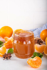 Golden sweet homemade tangerine jam, with spices and mint.  Sweet orange mandarin klementin jam or marmalade canning preserves in a jar, with whole and sliced tangerine on background