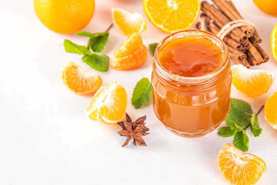 Golden sweet homemade tangerine jam, with spices and mint.  Sweet orange mandarin klementin jam or marmalade canning preserves in a jar, with whole and sliced tangerine on background