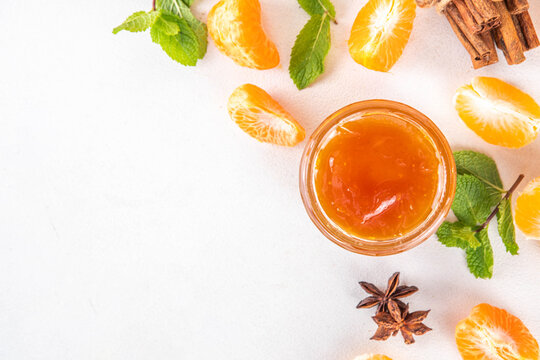 Golden sweet homemade tangerine jam, with spices and mint.  Sweet orange mandarin klementin jam or marmalade canning preserves in a jar, with whole and sliced tangerine on background