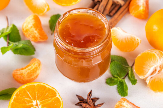 Golden sweet homemade tangerine jam, with spices and mint.  Sweet orange mandarin klementin jam or marmalade canning preserves in a jar, with whole and sliced tangerine on background