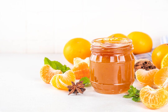 Golden sweet homemade tangerine jam, with spices and mint.  Sweet orange mandarin klementin jam or marmalade canning preserves in a jar, with whole and sliced tangerine on background