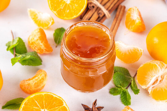 Golden sweet homemade tangerine jam, with spices and mint.  Sweet orange mandarin klementin jam or marmalade canning preserves in a jar, with whole and sliced tangerine on background
