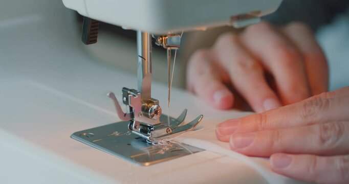 Close up of woman fingers sew on sewing machine. Details of sewing machine. Woman is overlocking textile. Workshop in sewing fabric. Creation and tailoring clothes.