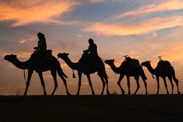 Silhouette of a caravan traveling through the desert at sunrise or sunset.