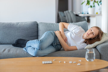 Young woman lying on sofa and suffering from abdominal pain at home