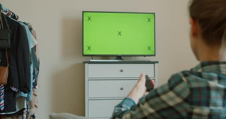 Television green screen, pretty girl watching modern TV at home and changing channels with remote control, movie and broadcasting. TV with horizontal green screen mock-up.