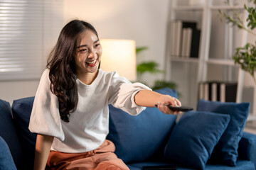 Young woman sitting on couch watching tv and holding a remote control