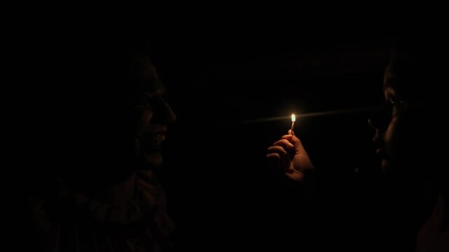 Young woman standing in darkness at attic in ruined house, lights up match sees mad man killer dressed as clown, scared expression. Halloween thriller concept.