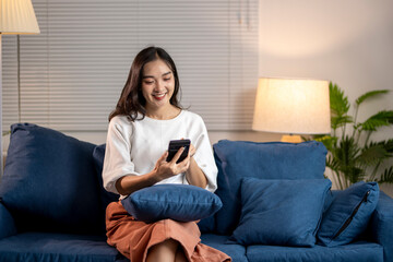 Fototapeta premium Young woman relaxing on sofa at home using smartphone browsing internet